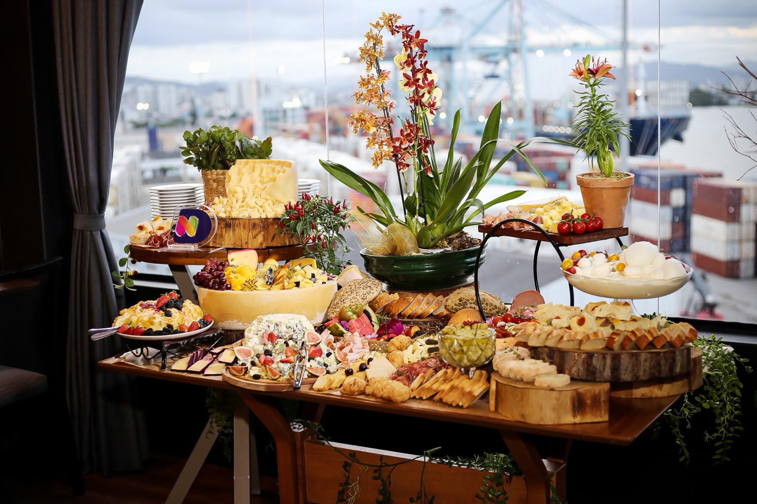 Mesa de frios de evento com gastronomia, flores e vista para o porto